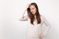 Portrait of preoccupied young woman in light clothes looking down, putting hand on head isolated on white wall