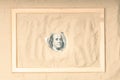 A portrait of the president peeking out from under the sand on a hundred dollar bill. around the dollars a wooden frame on the