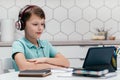 Portrait of preteen focused boy sitting near notebooks, looking at screen of tablet, having online lesson at home. Royalty Free Stock Photo