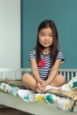 Adorable little asian girl child with long hair sitting in lotus position on bed in nursery at home