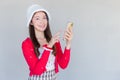 Portrait of a pretty Asian teen girl wearing a red dress and white hat happily smile using a smartphone on a white background Royalty Free Stock Photo