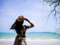 Asian woman wearing bohemian dress style with hat standing at coast looking to white beach and wave with blue sky