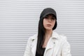 Portrait of a pretty attractive brunette young woman in a fashionable black baseball cap in a stylish white leather jacket Royalty Free Stock Photo