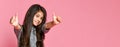 Portrait of a pretty attractive little girl in a dark dress, showing thumbs up with two hands on a pink background Royalty Free Stock Photo