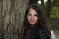 Portrait of a pretty, attractive woman in a leather blouson leaning against a tree trunk Royalty Free Stock Photo