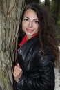 Portrait of a pretty, attractive woman in a leather blouson leaning against a tree trunk Royalty Free Stock Photo