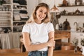 Portrait of pretty blond girl smiling and rejoicing while standing in stylish wooden kitchen at home