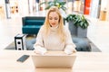 Portrait of pretty blonde businesswoman sitting on sofa in shopping mall typing working on laptop computer. Focused Royalty Free Stock Photo