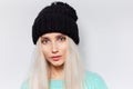 Portrait of pretty blonde girl with blue eyes on white background, wearing black hat and cyan sweater. Royalty Free Stock Photo