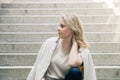 Portrait of a pretty blue eyed blonde girl sitting on the steps with her hand holding her neck Royalty Free Stock Photo