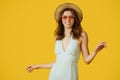 Portrait of pretty woman in summer dress, straw hat and colorful sunglasses posing and dancing on yellow background Royalty Free Stock Photo