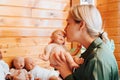 Portrait pretty caucasian young woman kissing realistic newborn baby doll sitting near collection of handmade kids toys Royalty Free Stock Photo