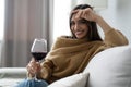 Pretty, attractive, stylish young woman sitting on couch having raised glass with red wine, examine, taste beverage