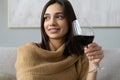 Pretty, attractive, stylish young woman sitting on couch having raised glass with red wine, examine, taste beverage