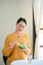 Pretty Asian woman enjoys eating healthy salad vegetables mix at dining table Royalty Free Stock Photo