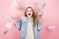 Portrait of pretty charming positive girl standing under shower from money having a lot of money in hands isolated on pink