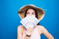 Portrait of pretty charming woman covering closing half face with fan from dollars looking out with eyes at camera isolated on blu Royalty Free Stock Photo