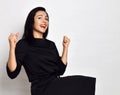 Portrait of Pretty cheerful brunette lady in stylish black dress sitting celebrating success with fists Royalty Free Stock Photo