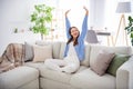 Portrait of pretty dreamy cheerful girl sitting on divan stretching yawning in light flat house apartment indoor