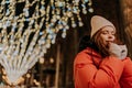 Portrait of pretty frozen young woman in hat and winter jacket warming hands in cold winter night standing posing on Royalty Free Stock Photo