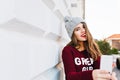 Portrait pretty girl with long hair in marsala sweater making selfie on grey wall background. She wears knitted hat and