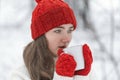 Portrait of pretty girl in red hat and mittens in snowy park. Cute young woman drink hot beverage from cup in winter outdoor Royalty Free Stock Photo
