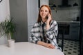 Portrait of pretty happy redhead female talking on smartphone sitting at kitchen desk. Smiling young woman holding Royalty Free Stock Photo