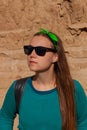 Portrait of pretty hipster girl in sunglasses, green sweatshirt, bandana standing on clay rock background on sunny day