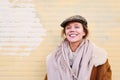 Portrait of a pretty hipster woman wearing hat outside smiling to camera. Yellow brick wall behind, daylight. Royalty Free Stock Photo