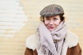 Portrait of a pretty hipster woman wearing hat outside smiling to camera. Yellow brick wall behind, daylight. Royalty Free Stock Photo