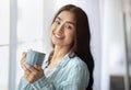 Portrait of pretty Indian lady standing near window with cup of hot drink, smiling at camera, indoors Royalty Free Stock Photo