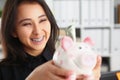 Pretty laughing young woman holding piggybank with banknote in it