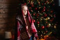 Portrait of pretty little blonde curly child girl wrapped in plaid looking at camera standing by decorated Christmas Royalty Free Stock Photo