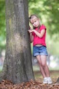 Portrait of a pretty little child girl standing near big tree trunk in summer park outdoors Royalty Free Stock Photo