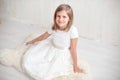 Portrait of pretty little girl in white dress , looking at camera and smiling, standing against gray background