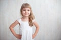 Portrait of pretty little girl in white dress , looking at camera and smiling, standing against gray background Royalty Free Stock Photo