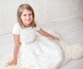 Portrait of pretty little girl in white dress , looking at camera and smiling, standing against gray background Royalty Free Stock Photo