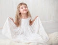 Portrait of pretty little girl in white dress , looking at camera and smiling, standing against gray background Royalty Free Stock Photo