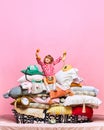 Portrait of pretty little princess sitting on big feather bed with pillows with retro phones over pink studio background