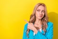 Portrait of pretty minded girl look direct finger empty space hesitate isolated on yellow color background