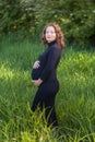 Portrait of pretty pregnant woman in a black dress green field park Royalty Free Stock Photo