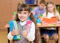 Portrait of pretty preschool girl with books in classroom showing thumb up Royalty Free Stock Photo