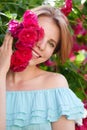 Portrait of a pretty redhead girl dressed in a white light dress on a background of blooming roses. Outdoor