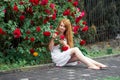 Portrait of a pretty redhead girl dressed in a white light dress on a background of blooming roses. Outdoor Royalty Free Stock Photo