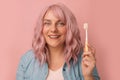 Portrait of pretty 20s 30s woman with curly pink hair, keeps toothbrush, cares of oral hygiene, over pink background Royalty Free Stock Photo