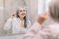 Portrait of pretty senior gray haired woman looking to mirror, cleansing her ears with a cotton swab in modern light Royalty Free Stock Photo