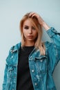 Portrait of a pretty sexy young blond woman in a denim jacket in a black dress near a vintage wall indoors. Royalty Free Stock Photo