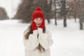 Portrait of pretty smiling girl in red knitted hat and mittens and woolen sweater on alley in winter park. Woman outdoor