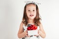 Portrait of smiling little girl in white dress with bow on head hold white gift box with red ribbon on white background Royalty Free Stock Photo