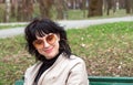 Portrait of a pretty smiling middle-aged woman sitting in the park on a bench in sun glasses with closed eyes Royalty Free Stock Photo